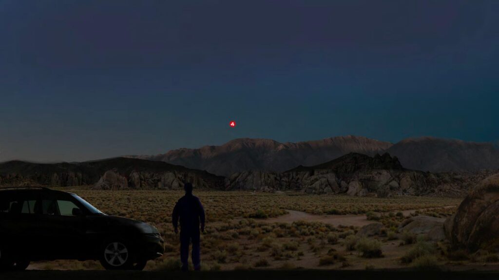 A digital rendering of a person standing in a desert landscape at night, with several red light sources visible in the s