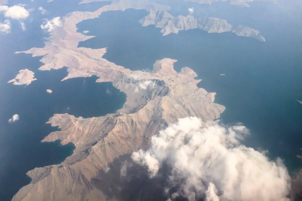 Redacted Pentagon mission report page titled DOW-UAP-D27 overlays a dark aerial view of the Gulf of Oman at dusk.